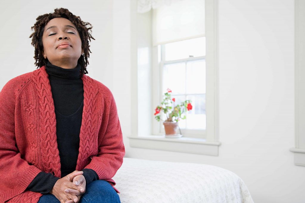 African-American woman sitting on edge of bed, eyes closed, resting and thinking