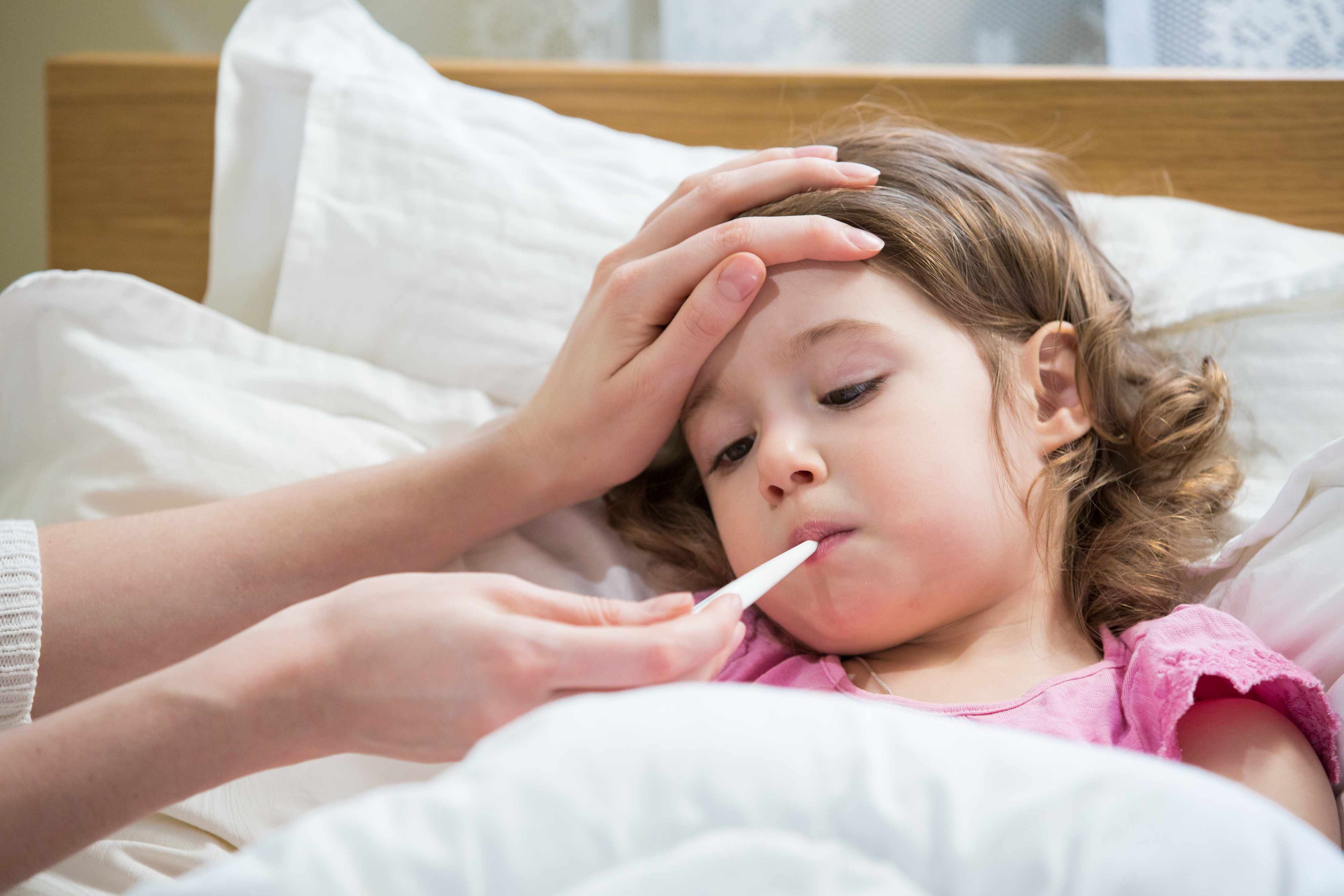 a sick child, a little girl in bed having her temperature taken with a thermometer