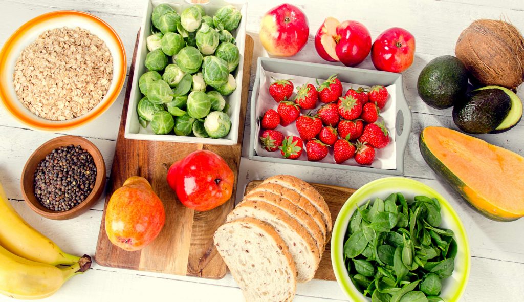 a variety of high-carbohydrate foods in bowls and on wooden surfaces, including fruits, vegetables and grains