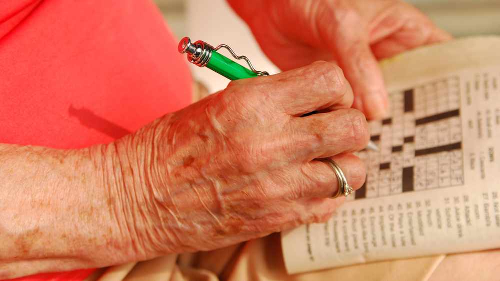 Acercamiento de la mano de una anciana que llena un rompecabezas con una pluma