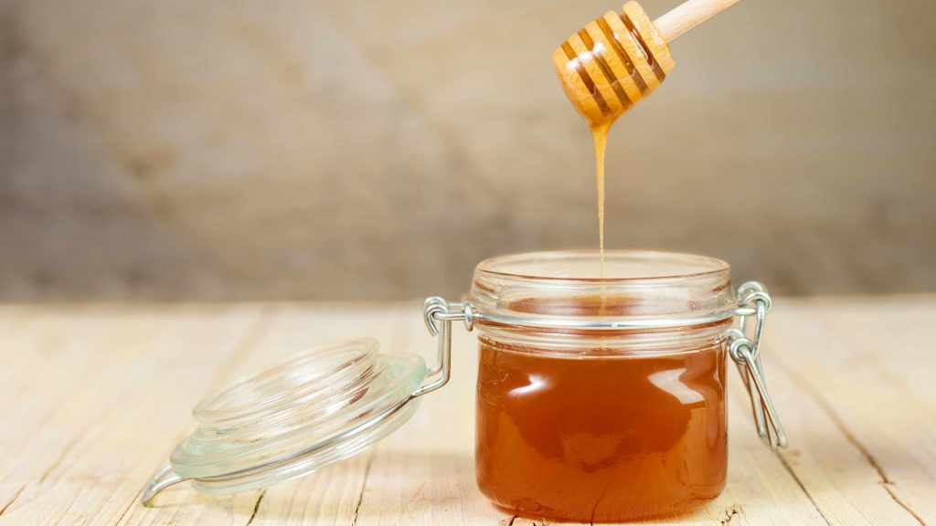 a jar of honey on a table with a wooden spindle