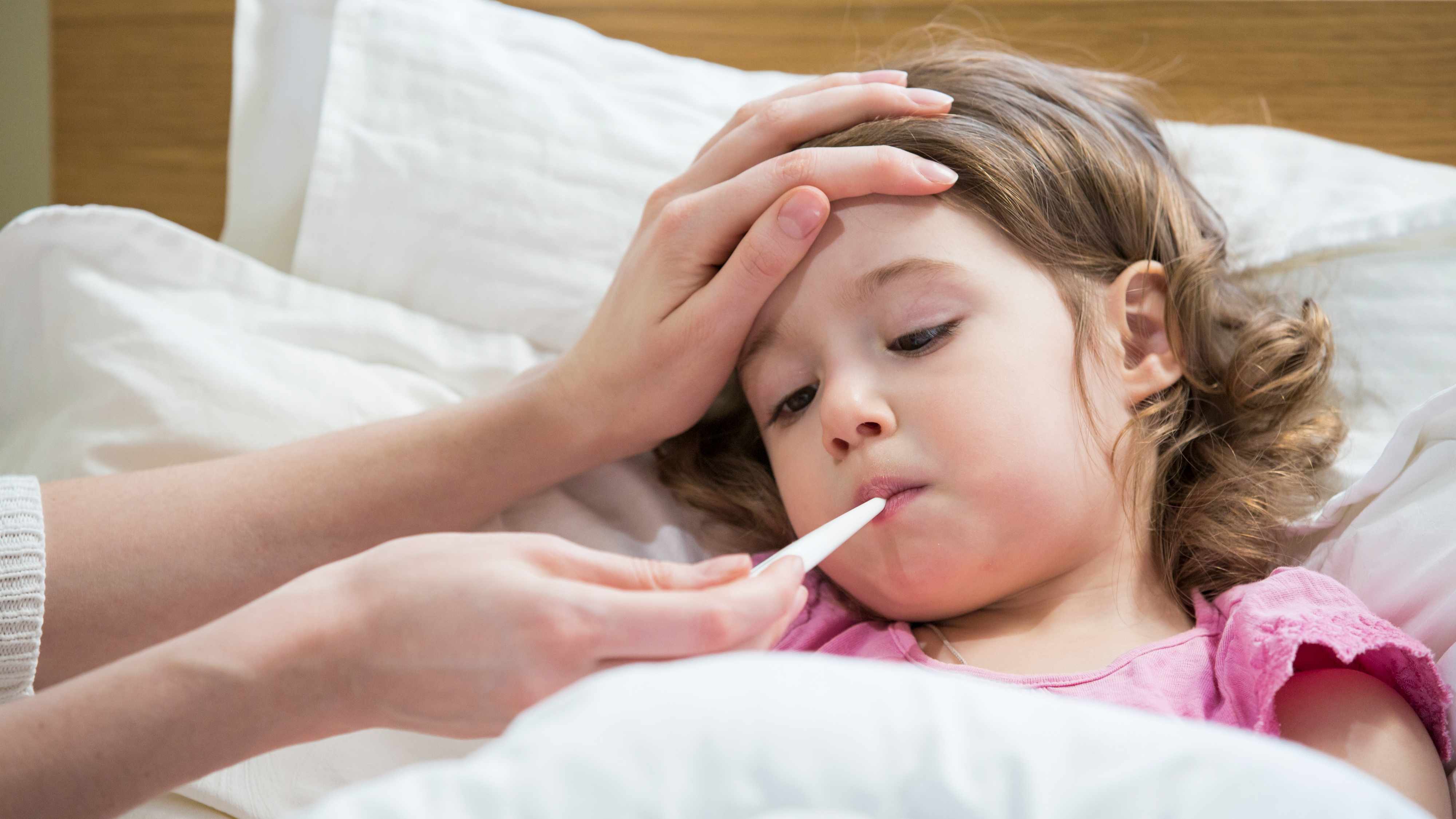 a little girl who is sick in bed with the flu or a cold and having her temperature taken