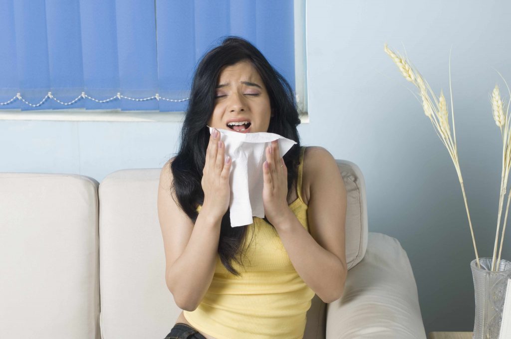 a young woman sitting on a couch, just about to sneeze