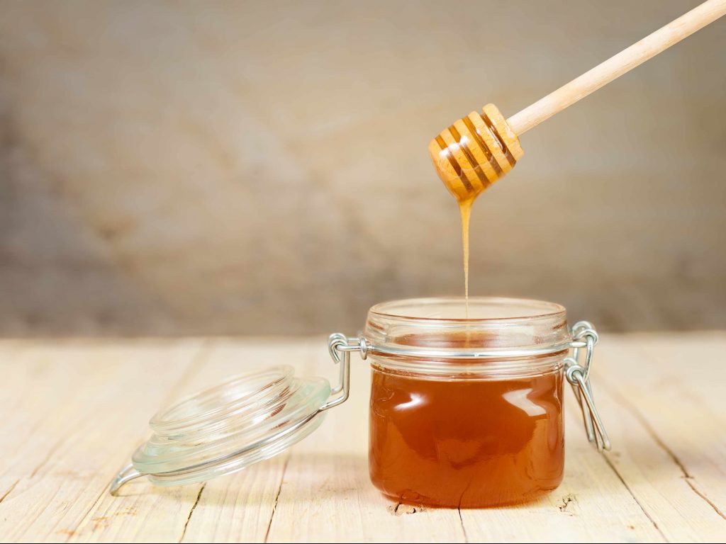 a jar of honey on a table with a wooden spindle