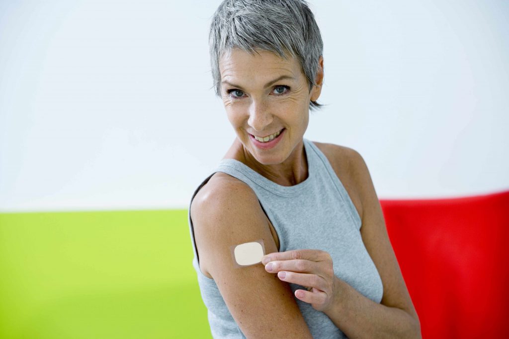 a smiling middle-aged woman with a nicotine patch on her upper arm