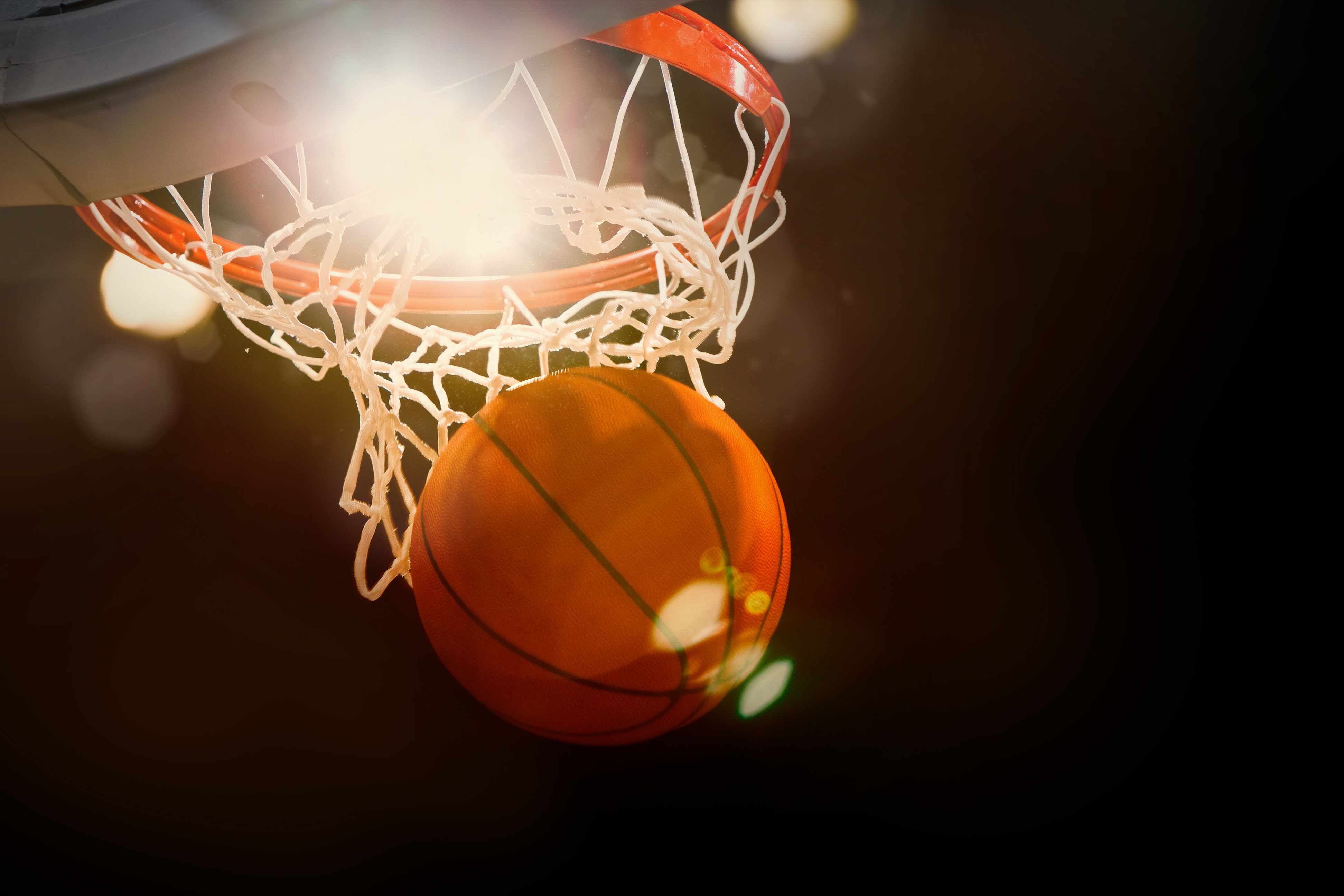 a basketball swooshing through a hoop with bright light in the background