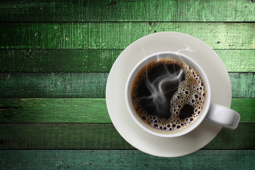 an overhead view of a single cup of steaming coffee on a green wooden surface