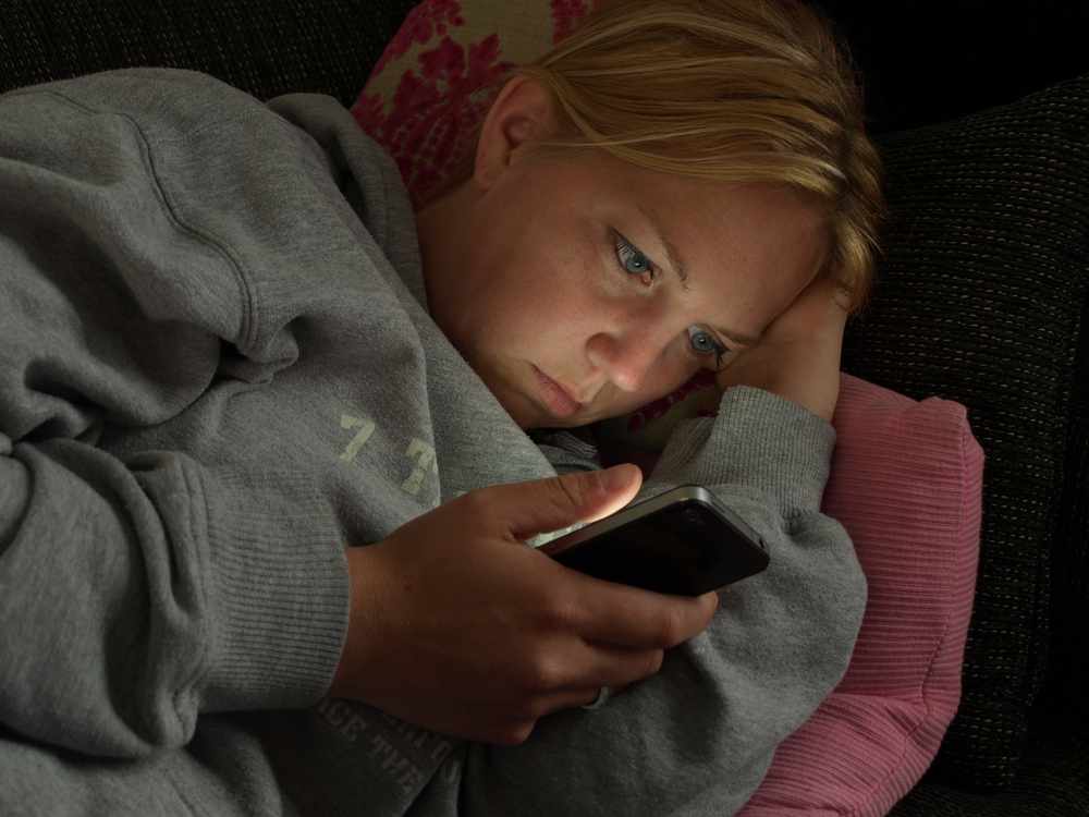A woman is browsing smartphone cell phone at night in bed