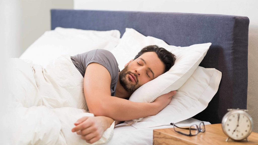 Un hombre duerme serenamente y en paz con un despertador delante