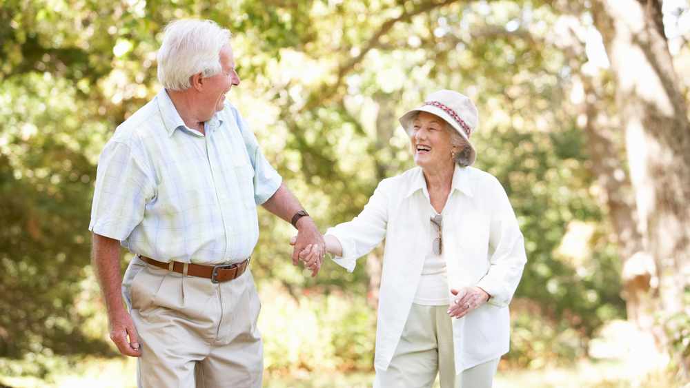 a smiling older couple, holding hands and walking outdoors