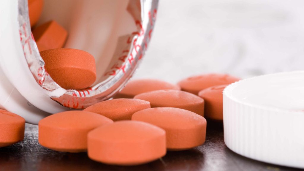 an open medication container spilling ibuprofen tablets out onto a table