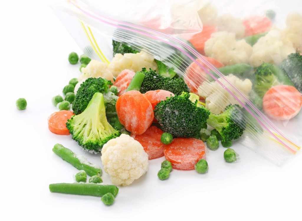 a plastic bag with frozen vegetables spilling out, carrots, peas, broccoli
