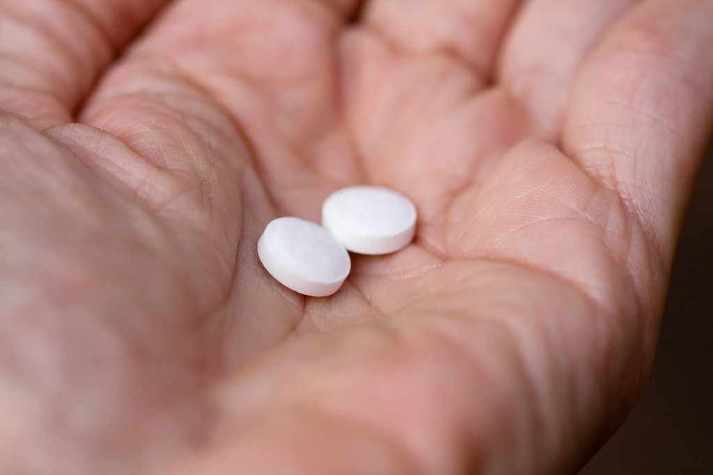 hand holding two aspirin tablets pills