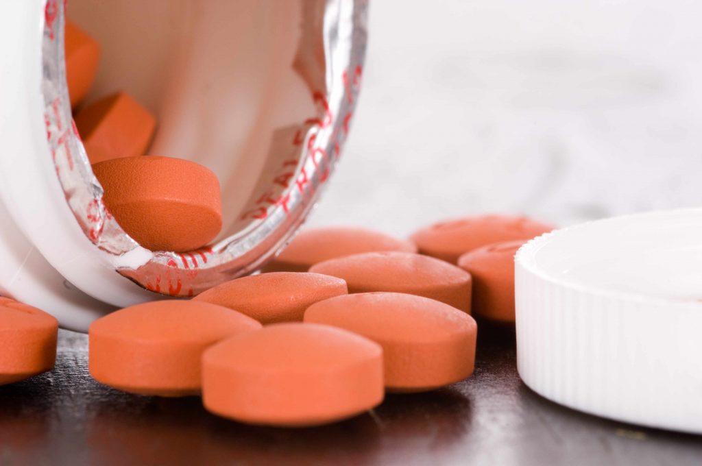 an open medication container spilling ibuprofen tablets out onto a table