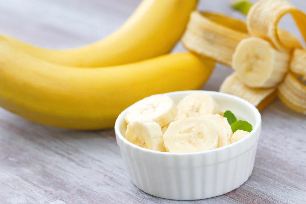 a bunch of bananas on a table and sliced bananas in a cup