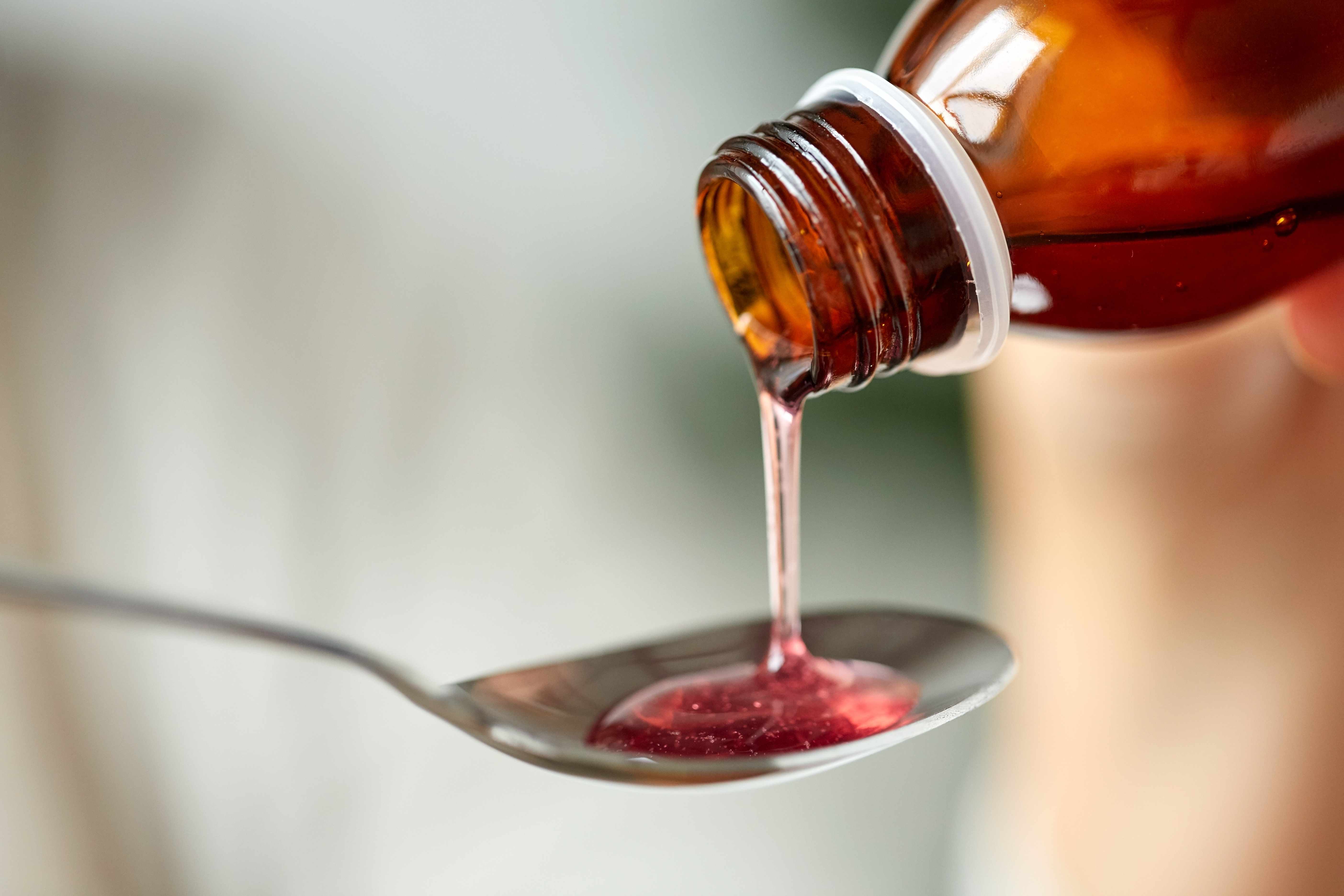 a bottle of cough medicine with the codeine syrup being poured onto a spoon