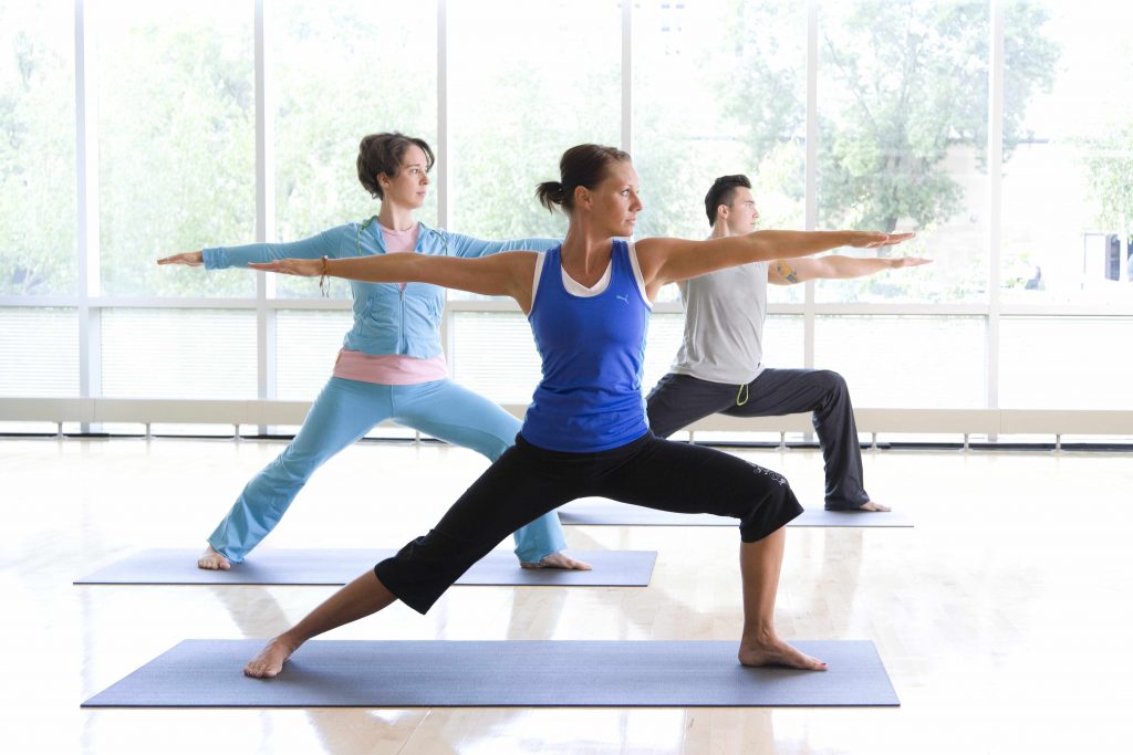 two women and a man doing yoga in front of a wall of windows in a sunny space