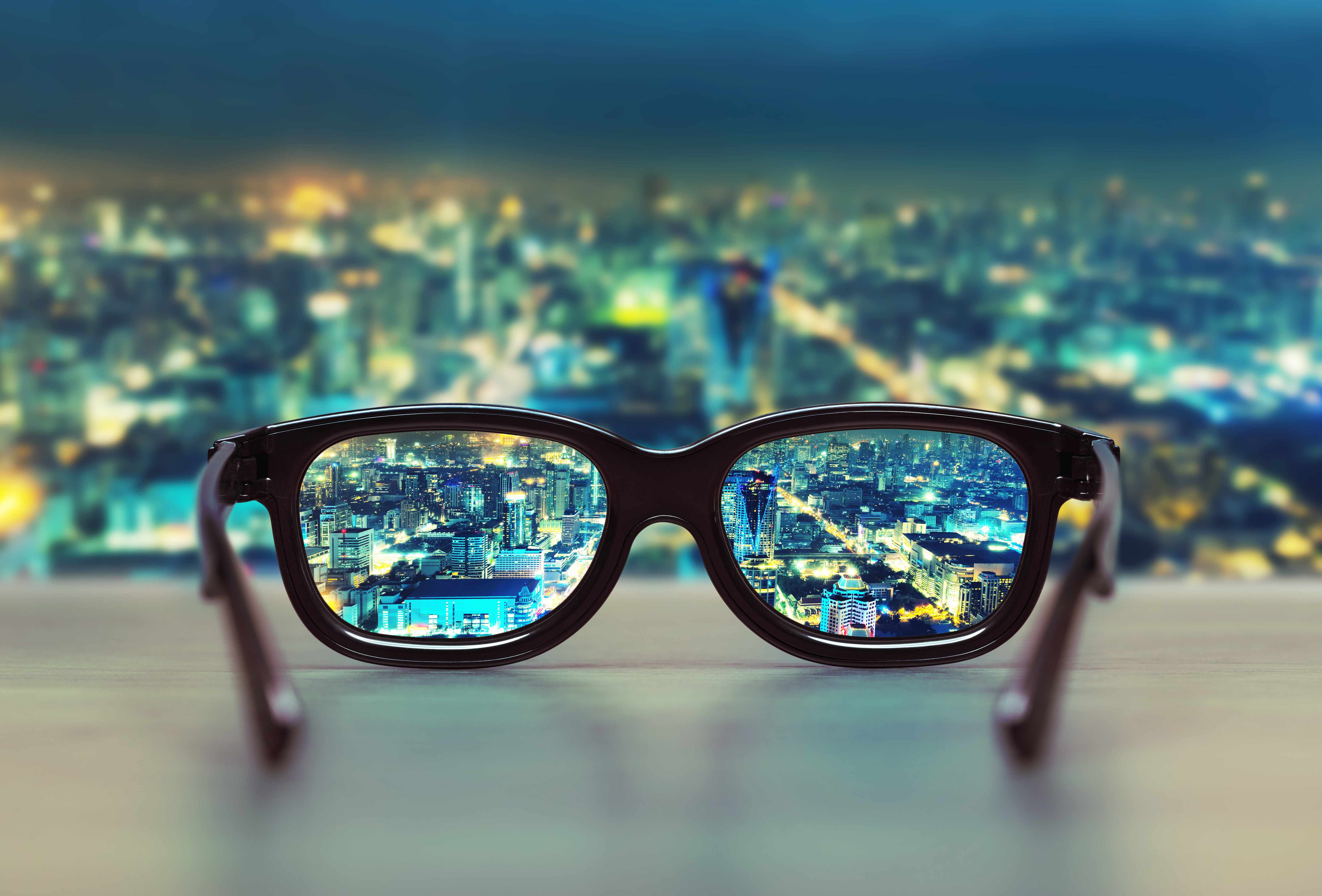 a pair of eye glasses on a windwosill with a night scene of a city in the background