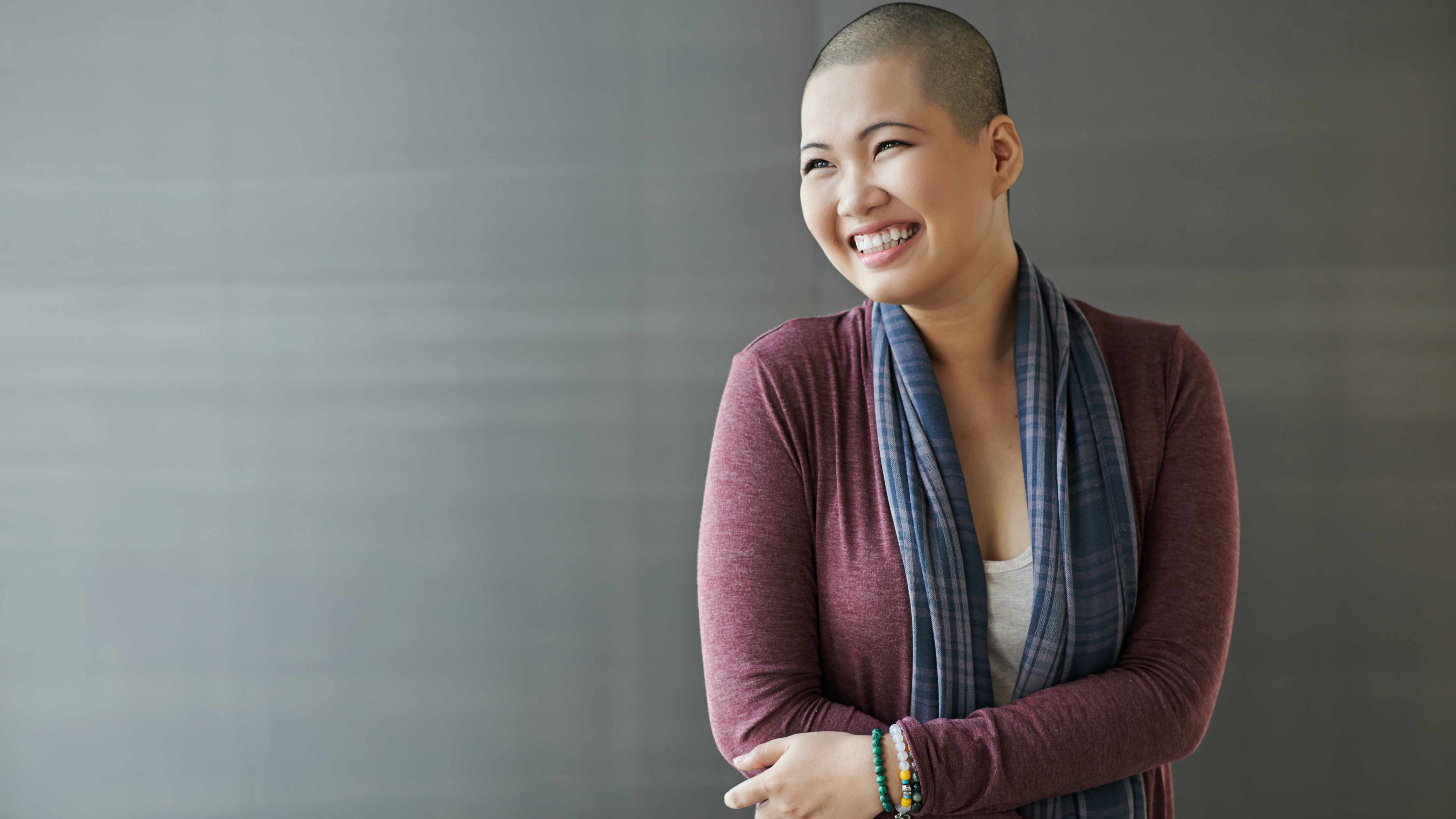 a smiling young Asian woman with shaven head representing cancer patient after chemo therapy