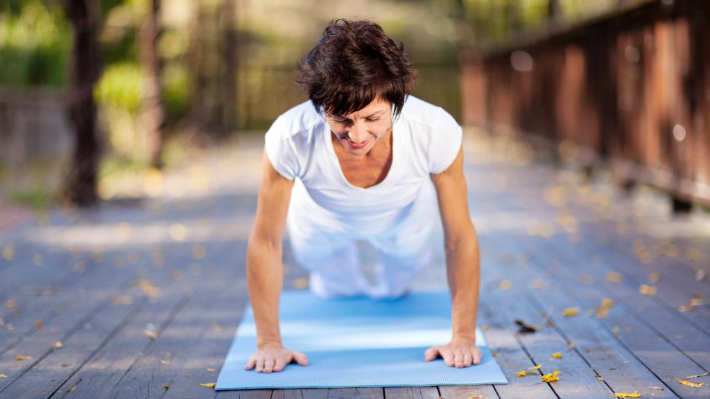 Mujer de mediana edad sobre una colchoneta de yoga en pleno ejercicio y estiramiento 