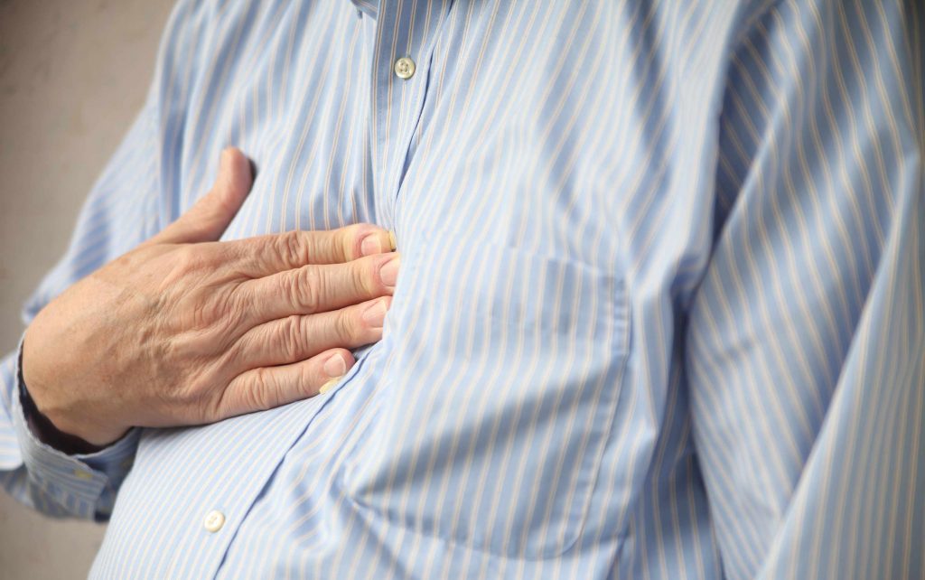 man holding his hand to his chest in pain maybe having a heart attack or heartburn