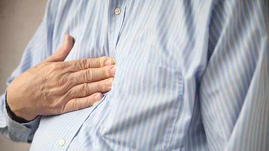 Un hombre se sostiene el pecho con la mano porque siente dolor, tal vez debido a un ataque cardíaco o a acidez estomacal