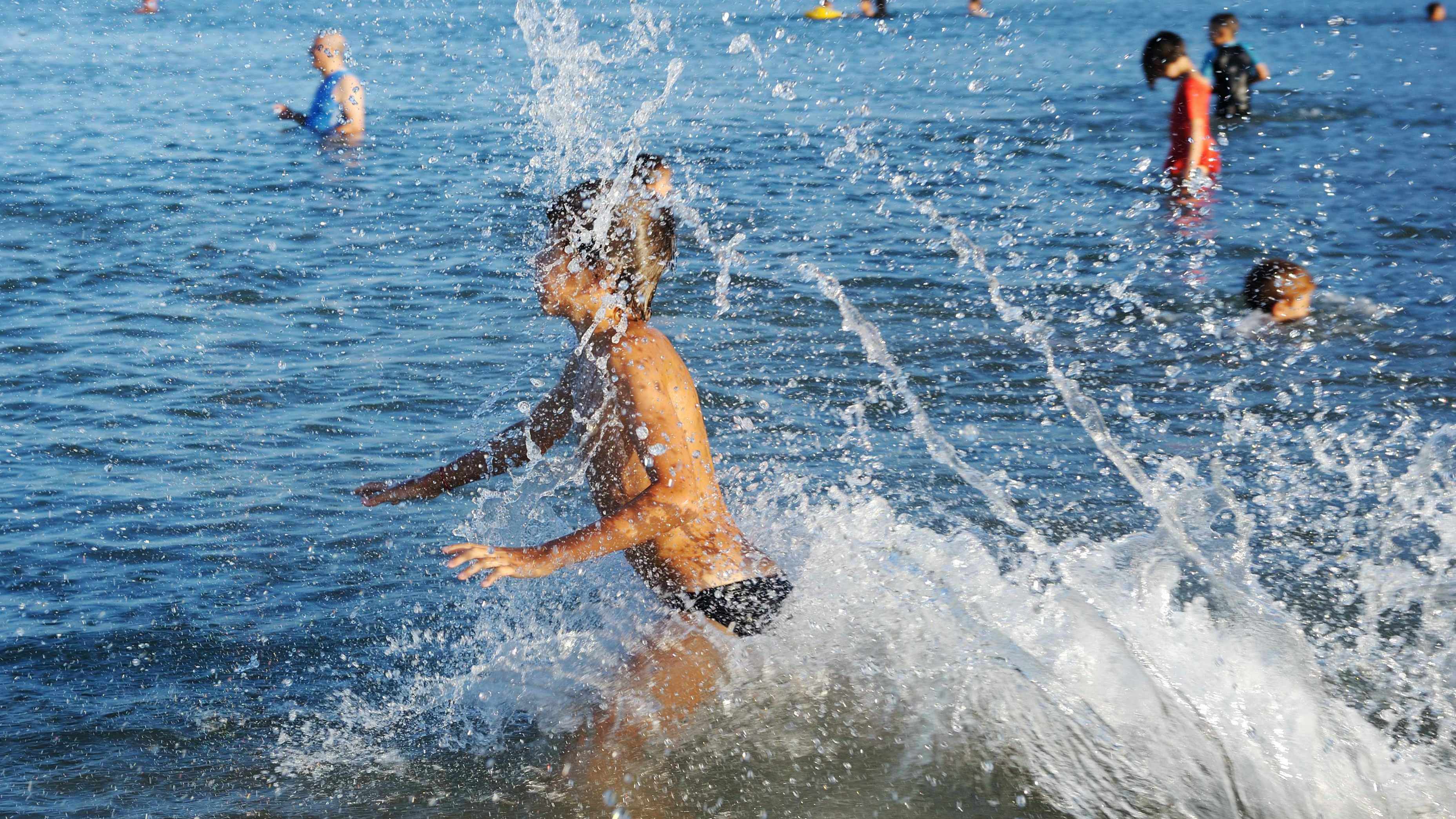 people in lake water swimming and a young child splashing through the water