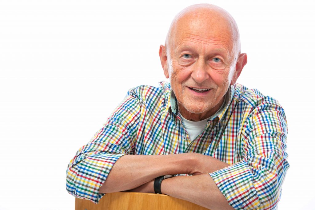 a close-up of a bald, friendly-looking older man in a plaid shirt