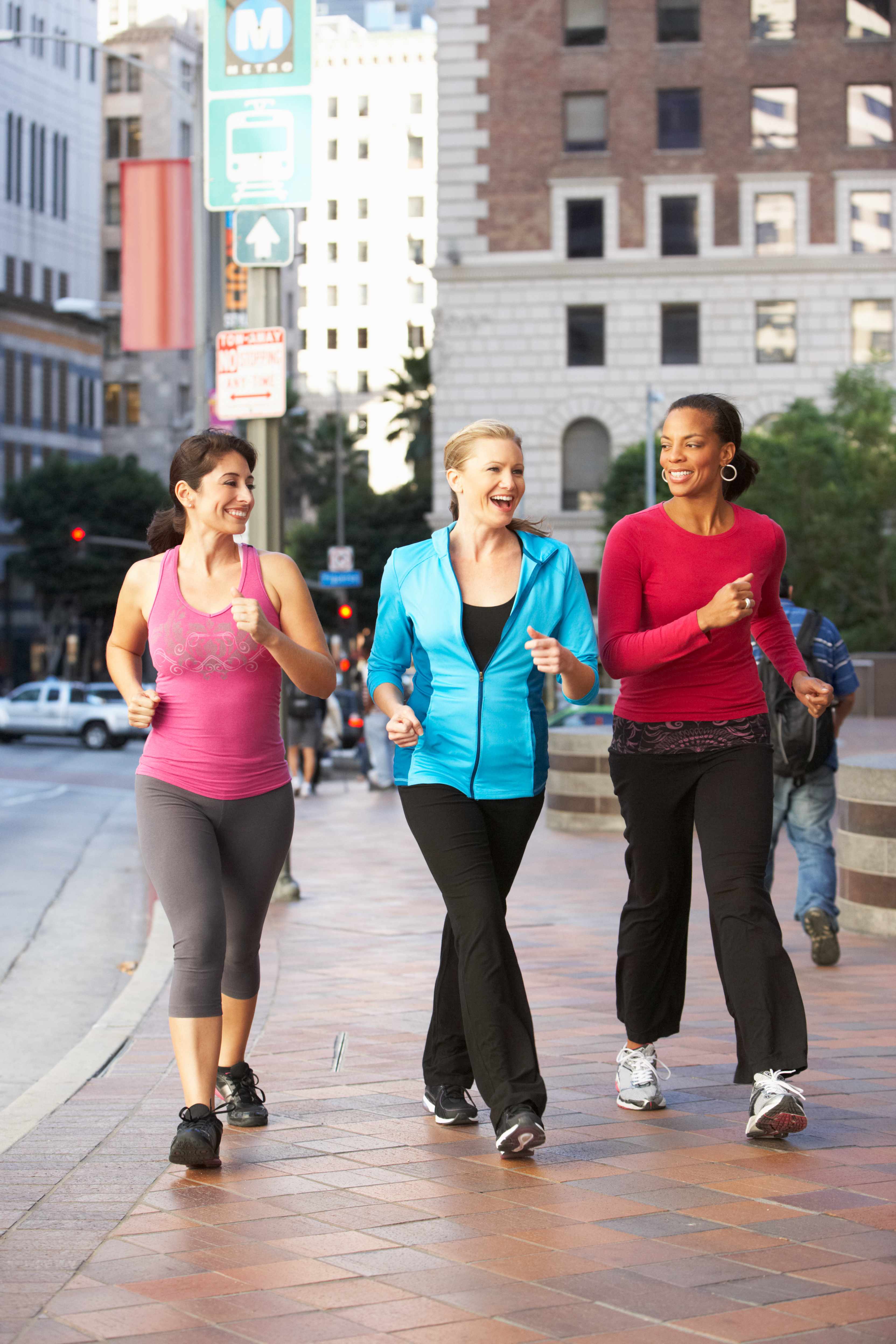 three smiling young women walking vigorously along a city sidewalk
