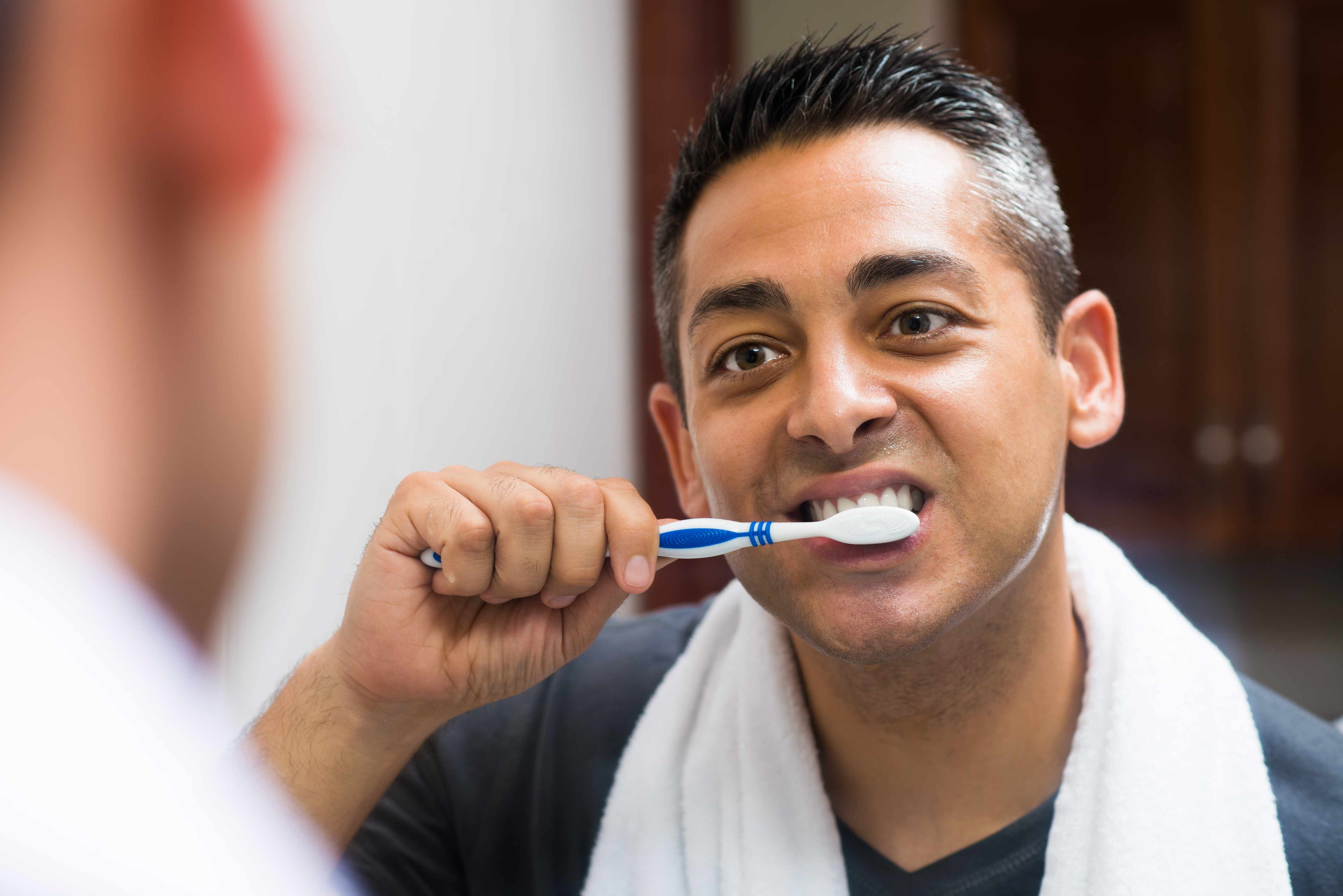 a man looking in a bathroom mirror and brushing his teeth