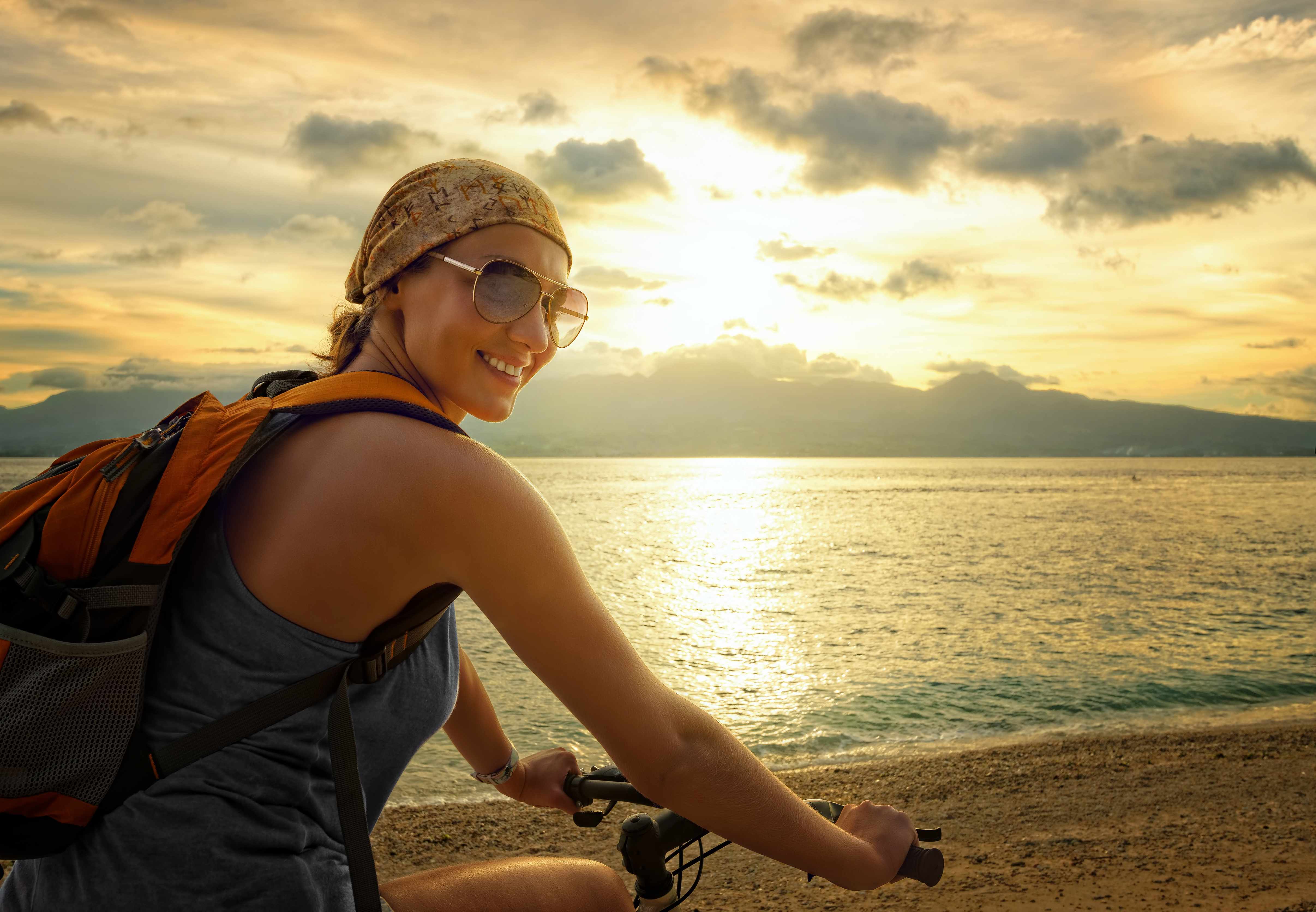 a young woman riding a bicycle along the beach or lake shore with the sun setting