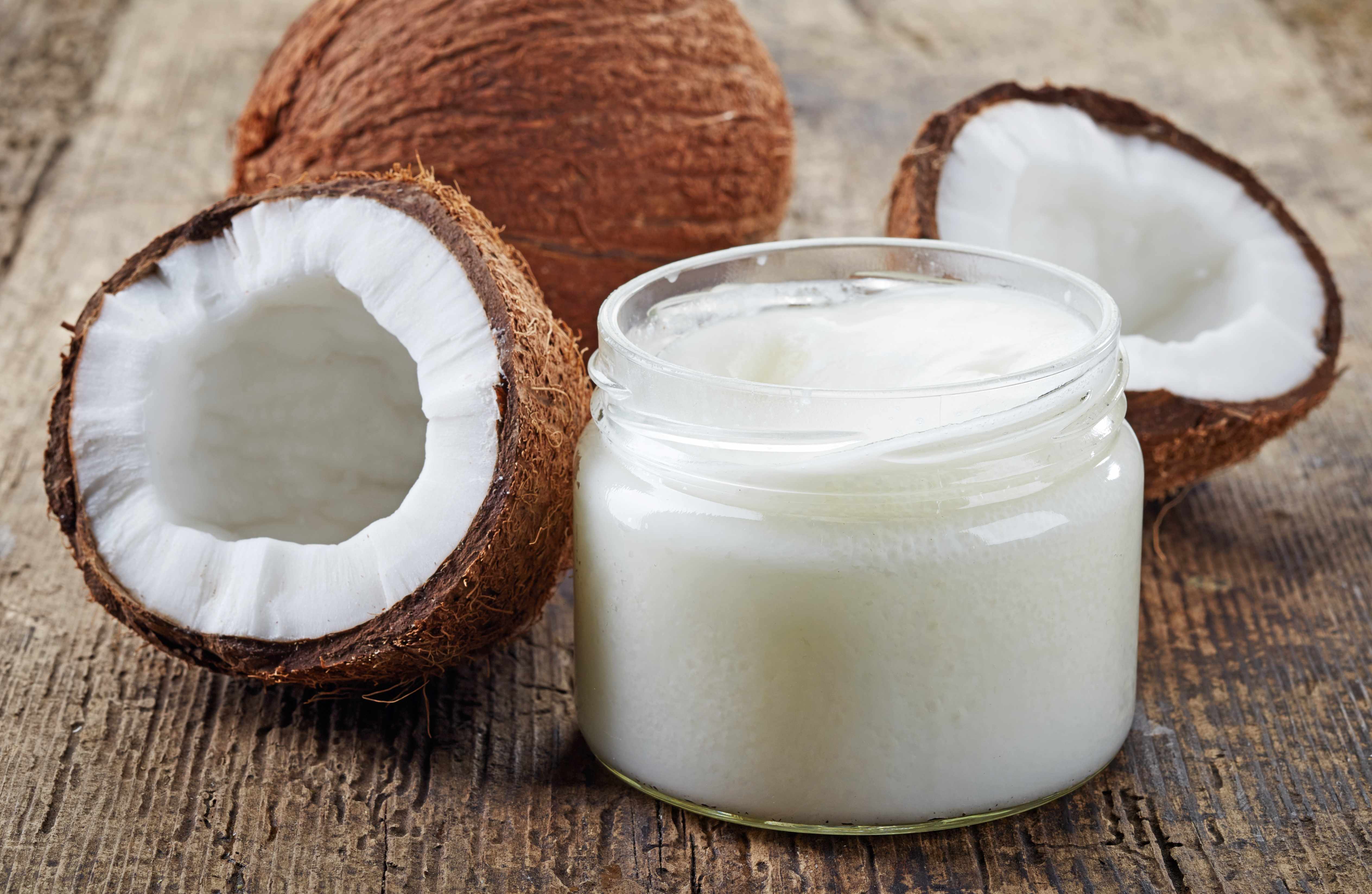 a coconut cut in half, sitting on a wooden table with a jar of coconut oil or butter