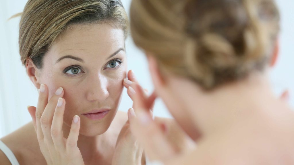 a woman looking in a mirror touching her face and looking for wrinkles