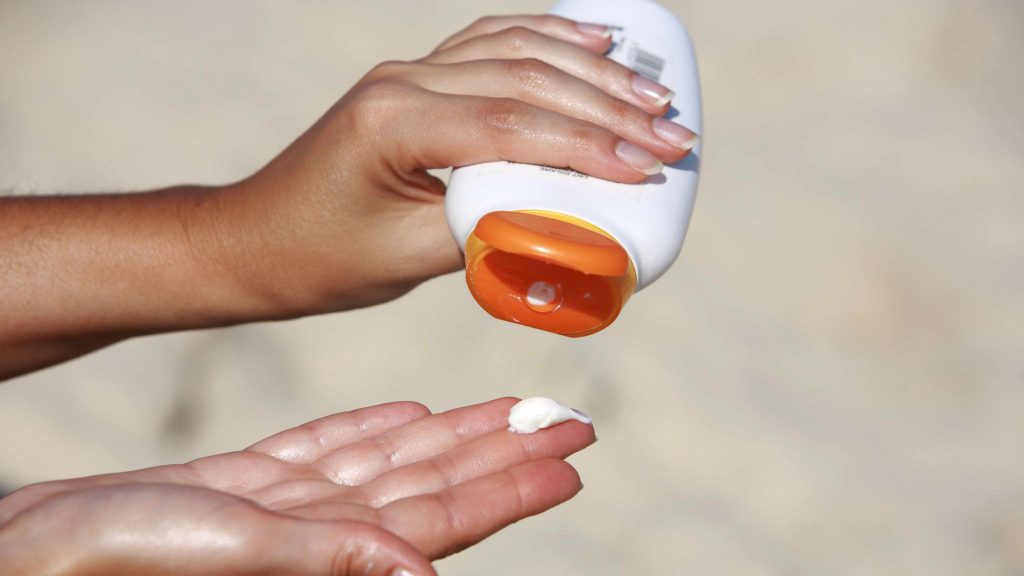 a woman squirting lotion or sunscreen out of a bottle onto the tip of her fingers