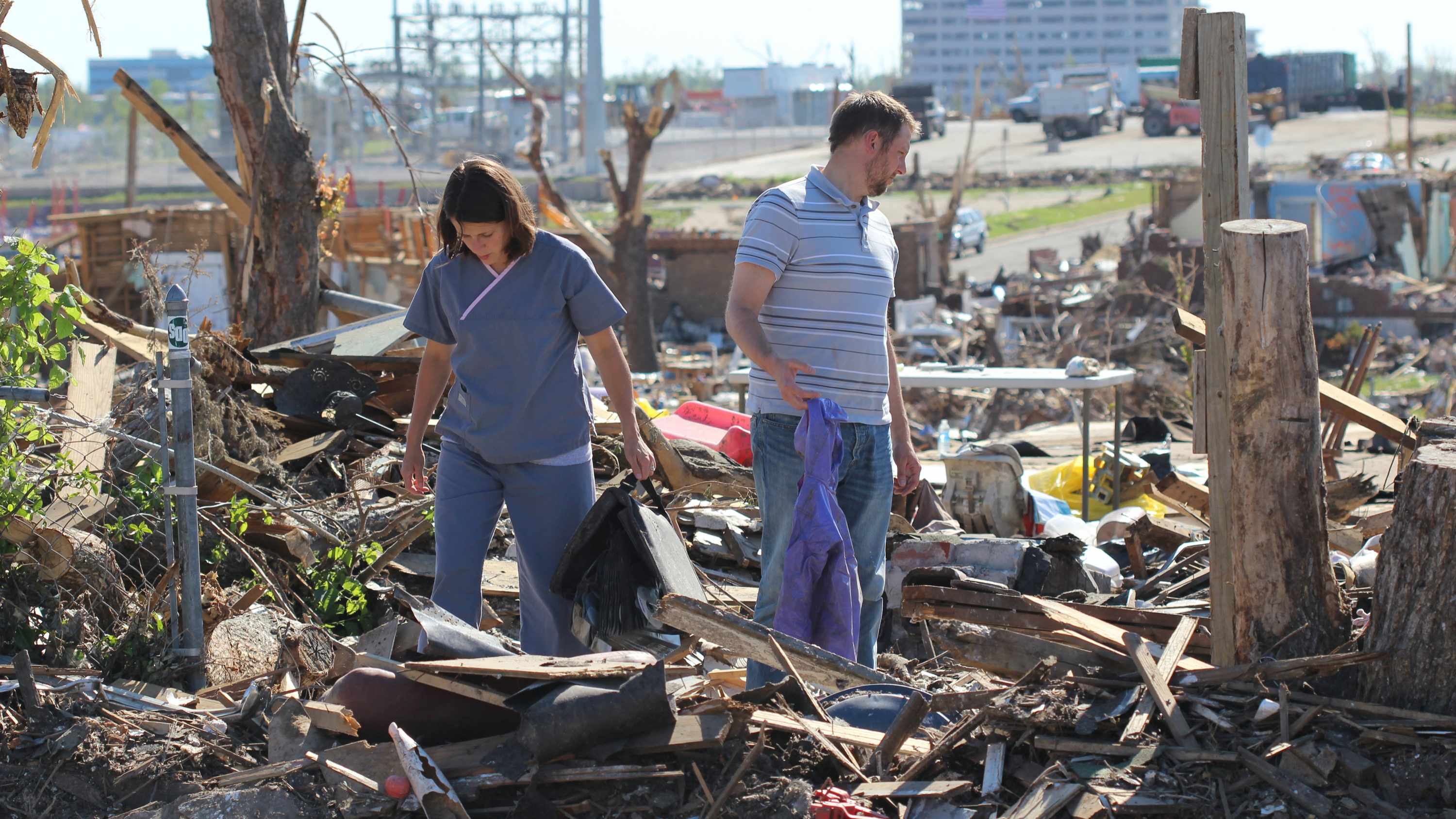 a young couple walking through debris from their home after a storm