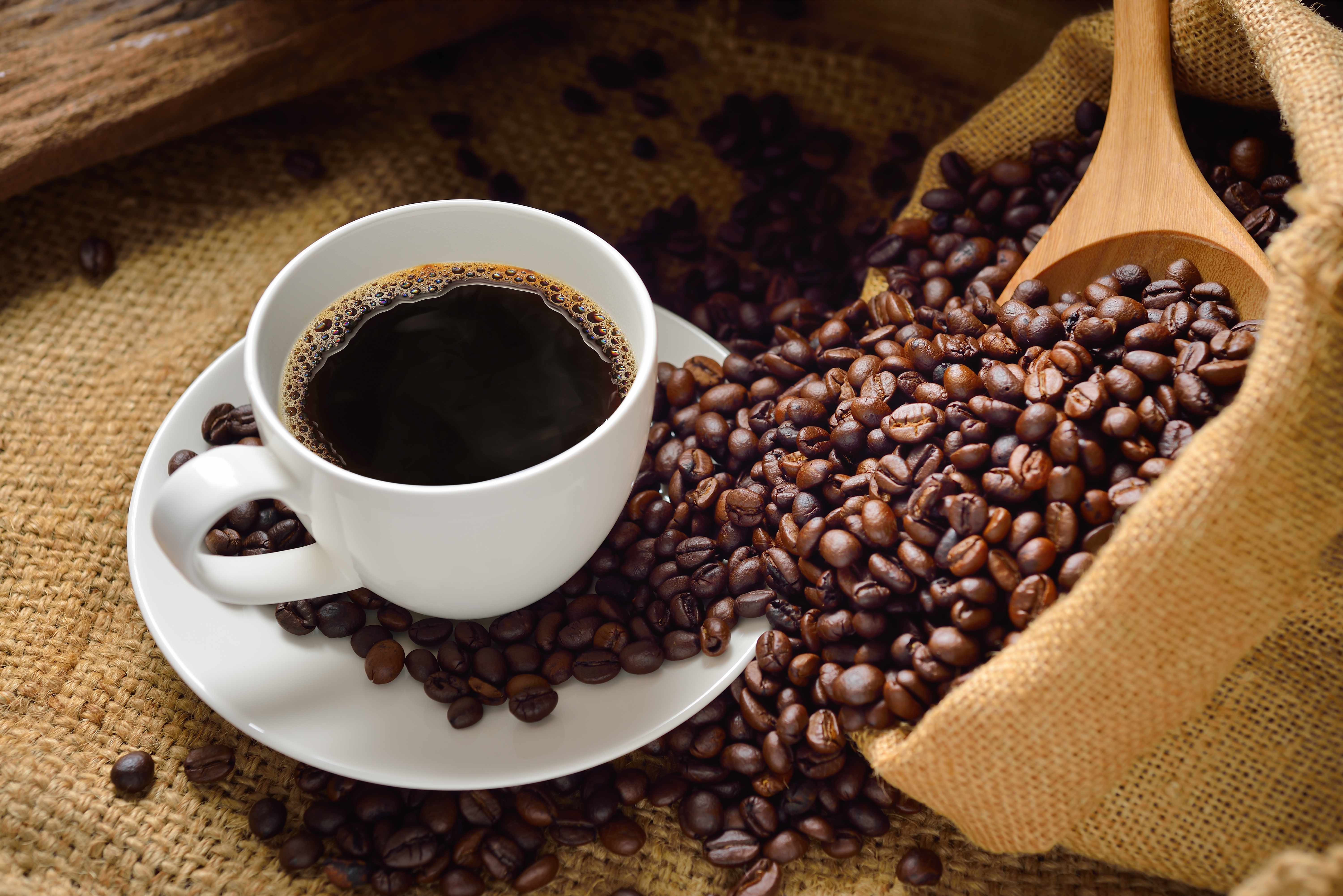 a cup of coffee on a burlap cloth and coffee beans spilling around the table