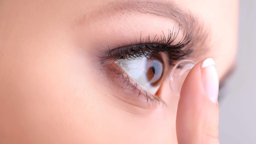 un primer plano de una mujer joven insertando una lente de contacto en su ojo