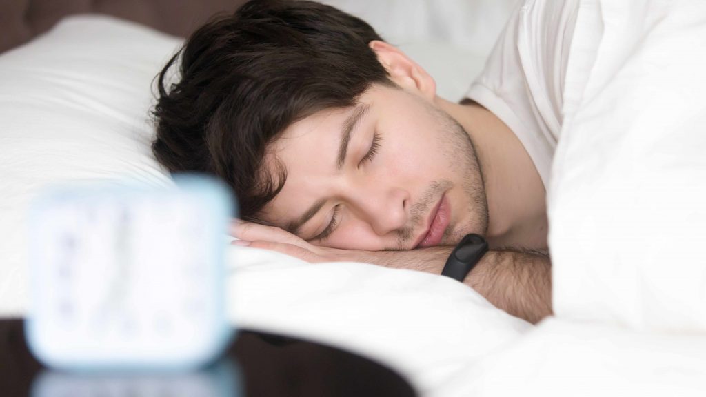 Un hombre dormido en la cama con un medidor de actividad física en la muñeca