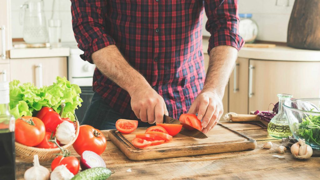 a man in a kitchen cutting tomatoes and other healthy vegetables for a salad dish
