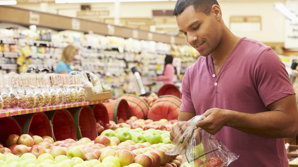 a young African-American man grocery shopping in a store for healthy food, picking fruits for his bag