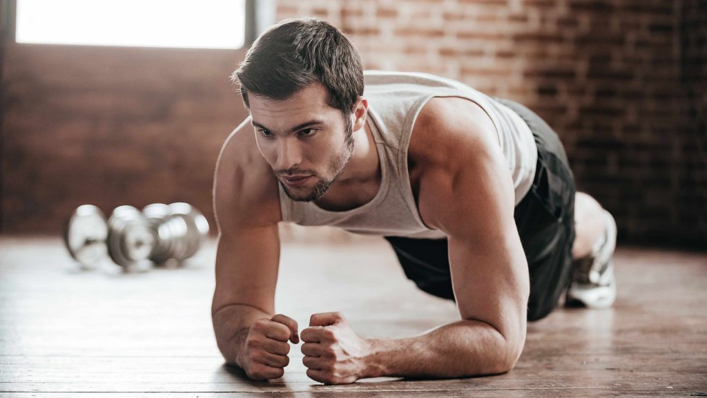 a young man in a gym, doing plank exercises for core muscle muscle development