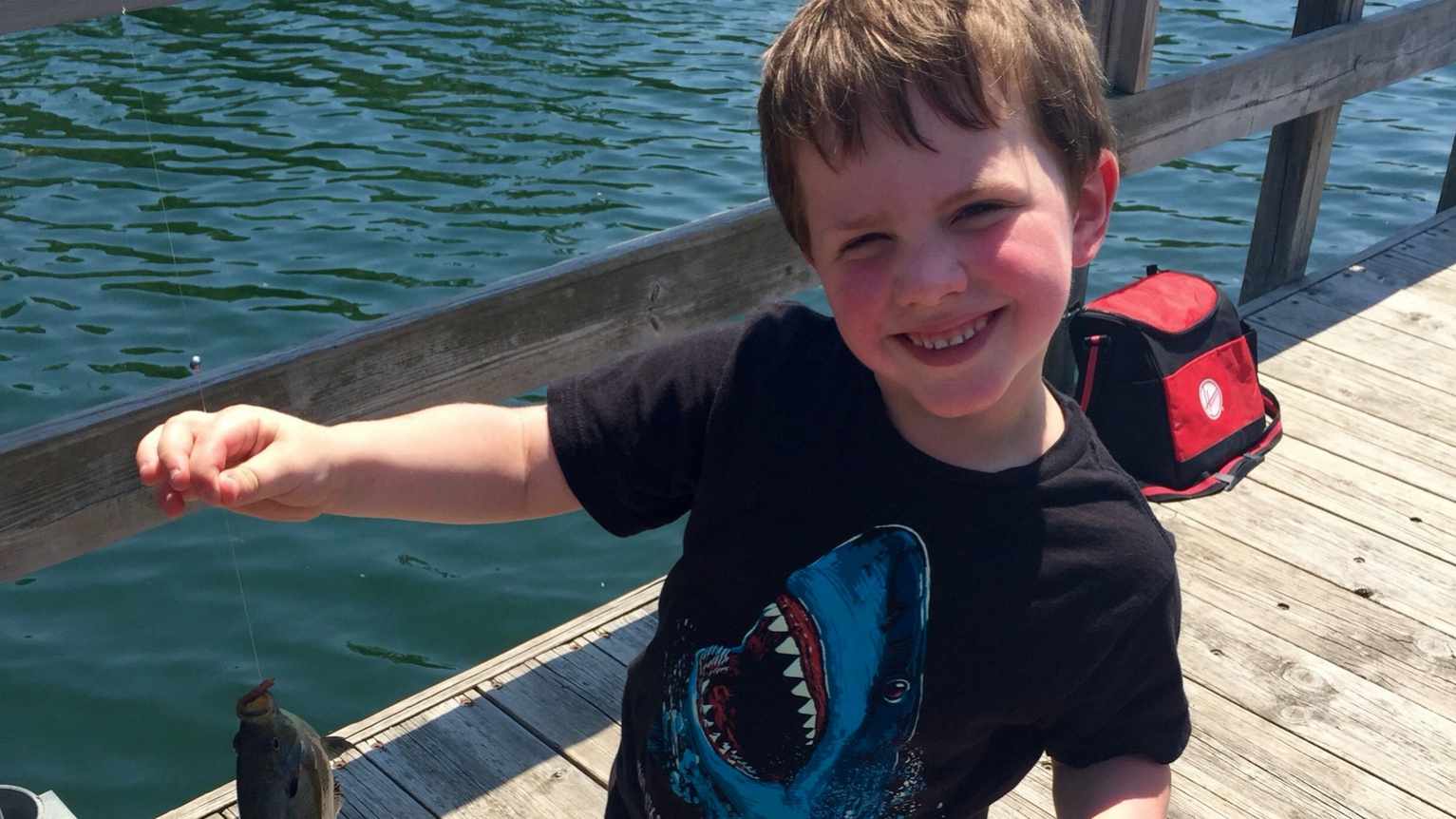 patient Gus on a fishing dock smiling and holding a fish