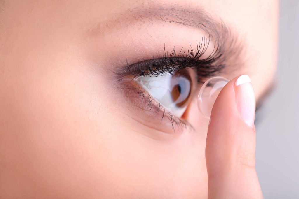 a close-up of a young woman inserting a contact lens into her eye