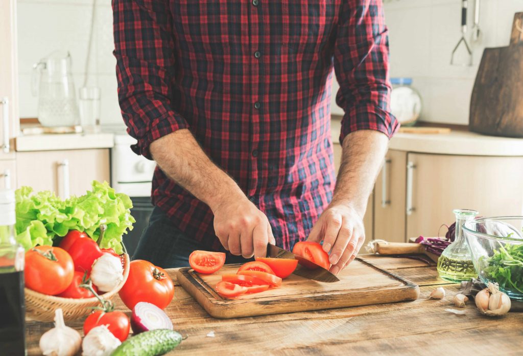 a man in a kitchen cutting tomatoes and other healthy vegetables for a salad dish