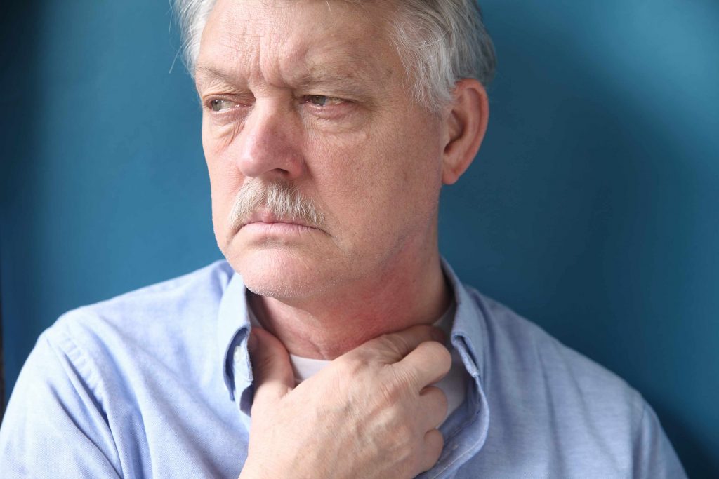 a close-up of an older man with his hand to his throat, looking very uncomfortable, perhaps feeling something is stuck in his throat