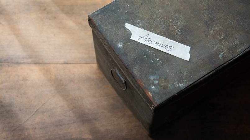 an old metal filing box for documents with a piece of tape that says 'Archives'