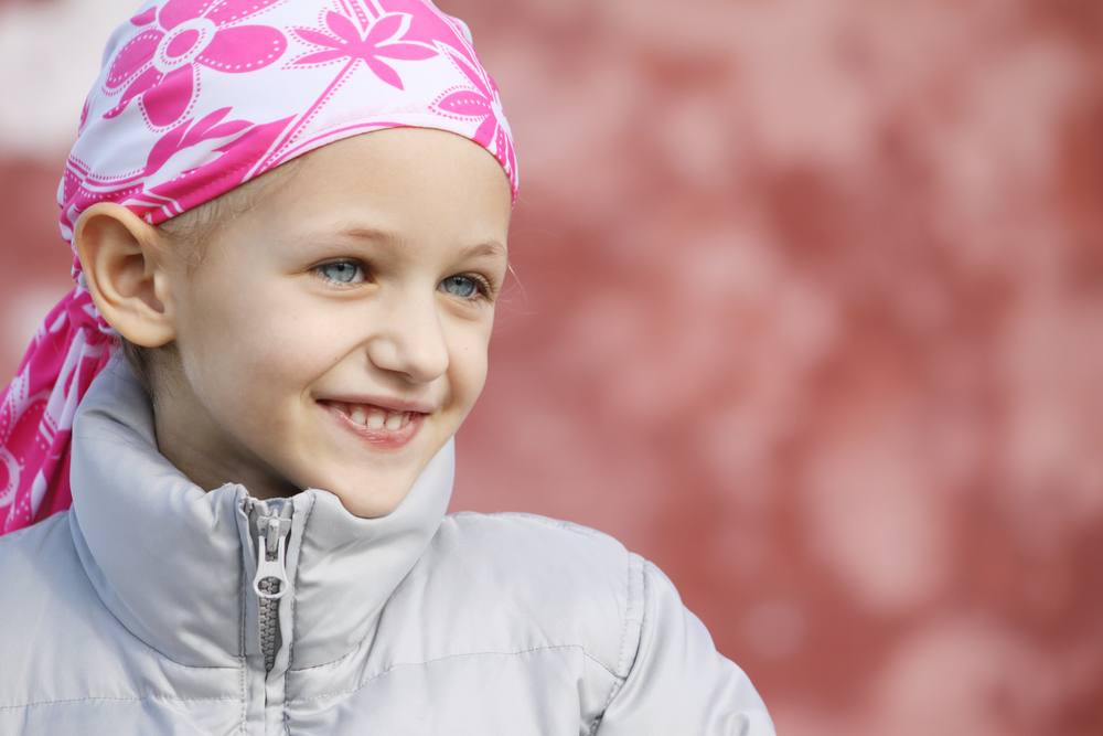 young girl with cancer wearing a bandana and smiling