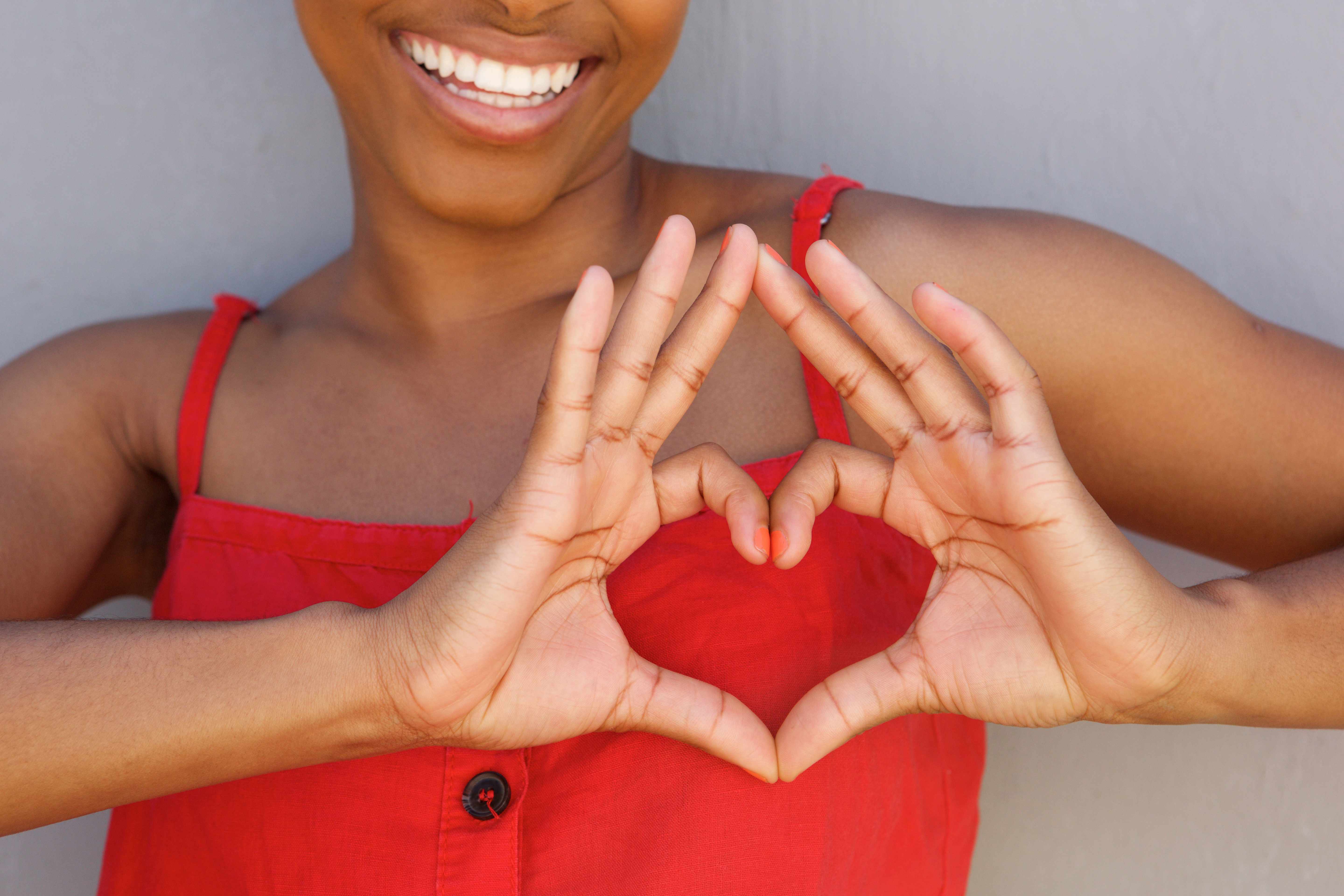 an African-American woman in a red shirt smiling and forming her hands in the shape of a heart