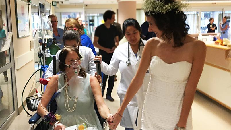 patient Amy Cierzan-Shaw and her daughter Alison in her wedding gown, holding hands in the hospital hallway 