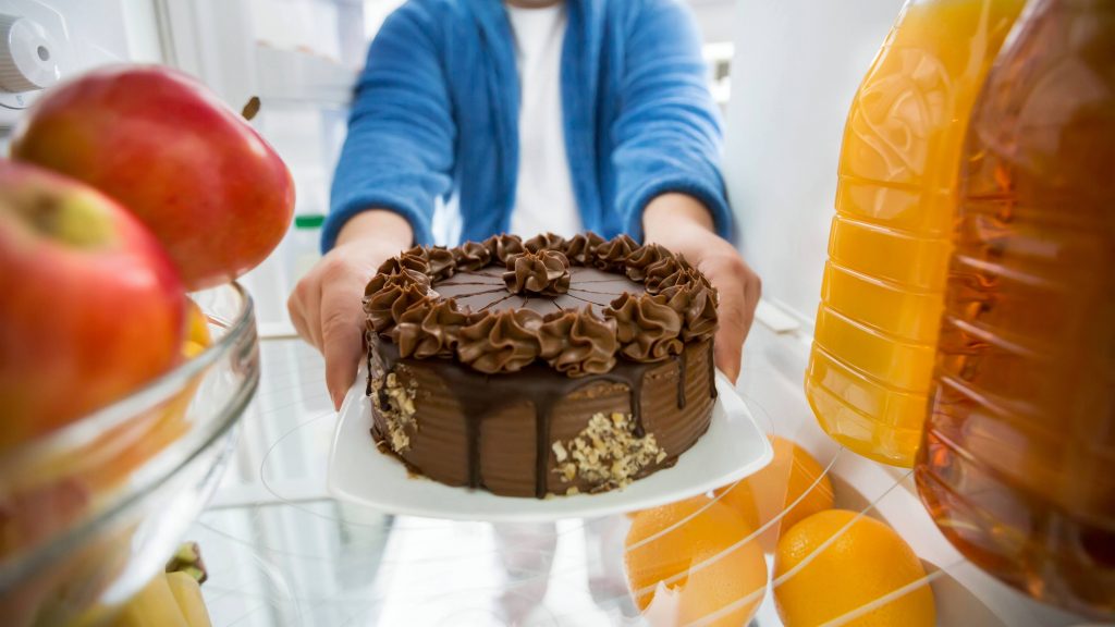 a person pulling a sweet dessert, a large chocolate cake out of the refrigerator
